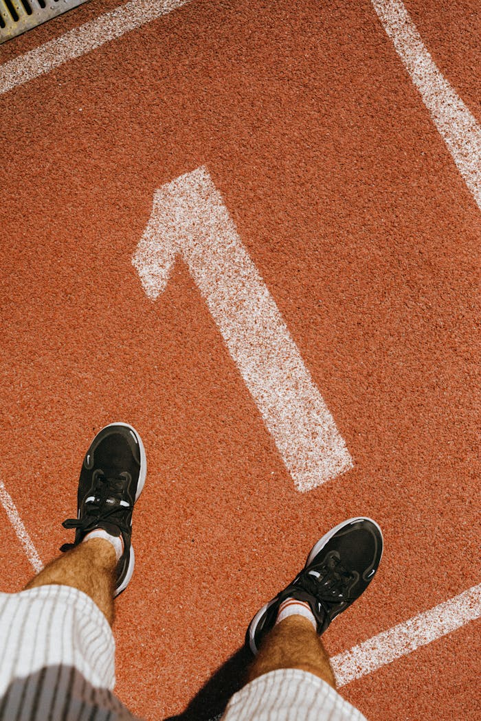 Man standing on number one lane of outdoor running track wearing sports shoes.